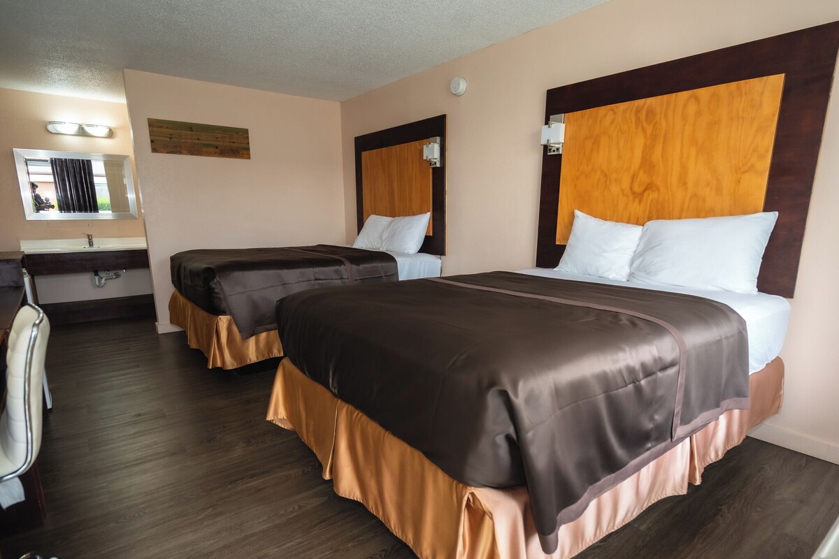 A hotel room with two beds, a desk, and a bathroom.