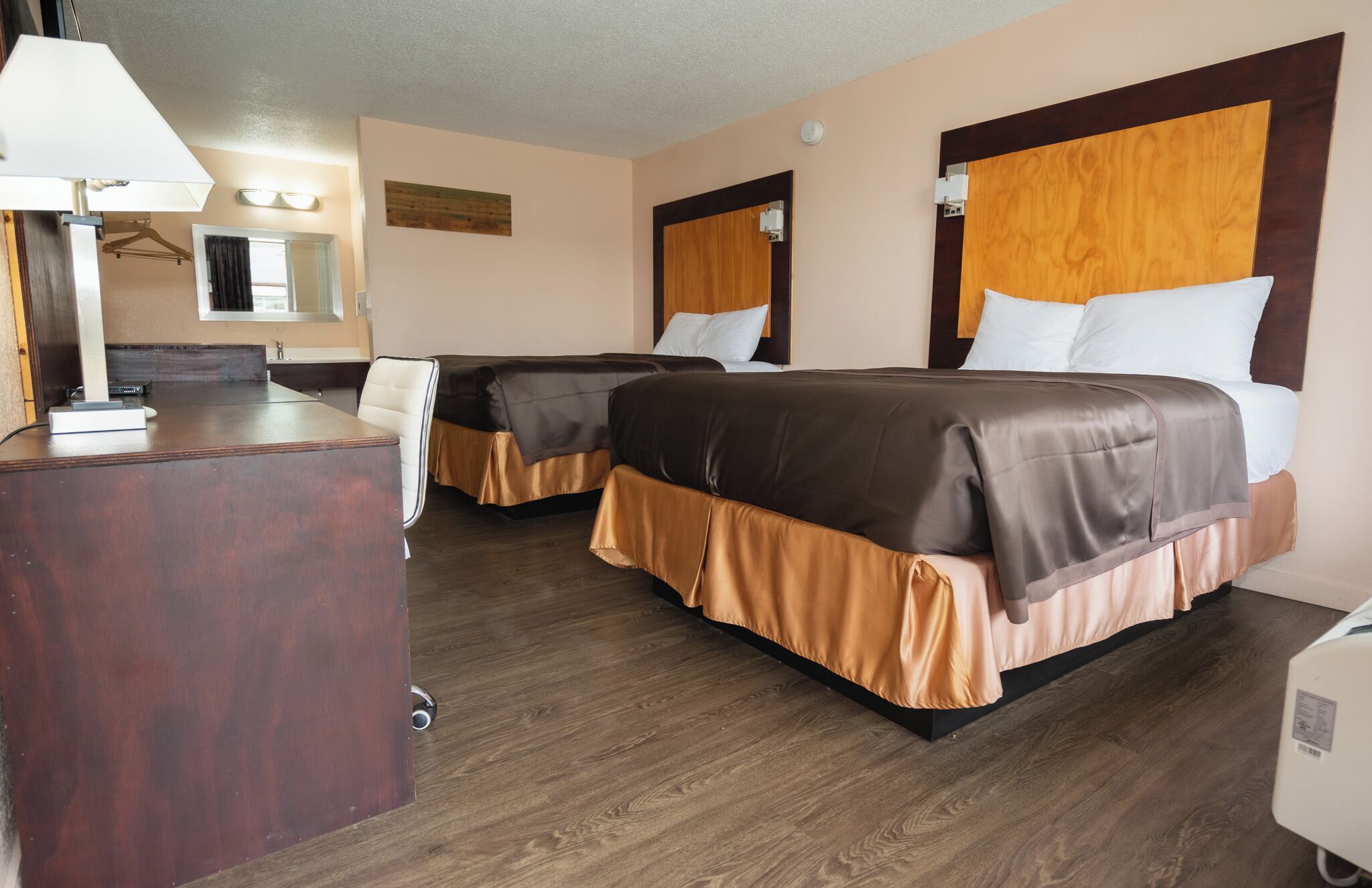 A hotel room with two beds, a desk, and a lamp.