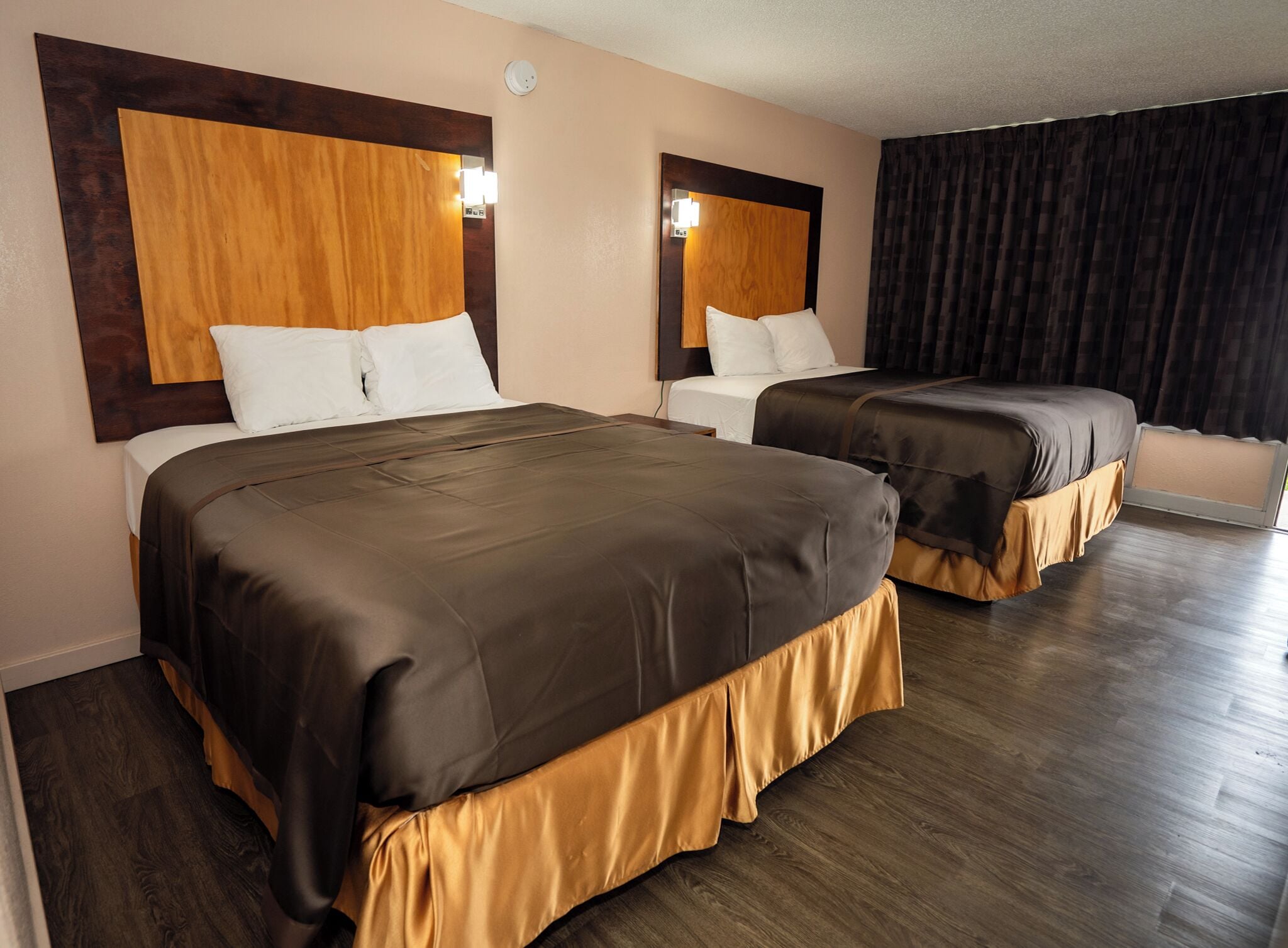 A hotel room with two beds, wooden headboards, and a large window with curtains.