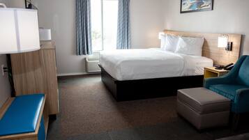 A hotel room with a bed, a desk, a chair, and a bedside table.