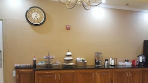 Una cocina con armarios de madera, un reloj y un mostrador tipo buffet con diferentes alimentos.