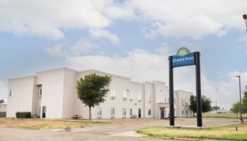 A Days Inn by Wyndham with a flat-roofed, single-story building, a parking lot, and a clear sky.