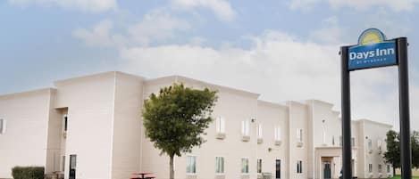 Et Days Inn by Wyndham hotel med en flad, etetages bygning, en parkeringsplads og en klar himmel.