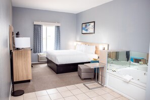 Una habitación de hotel con cama, mesita de noche, lámpara y un espejo grande.