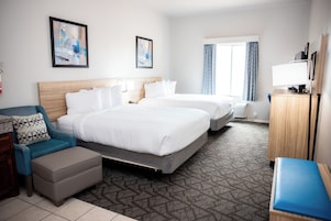 A hotel room with two beds, a desk, a chair, a sofa, and artwork on the walls.
