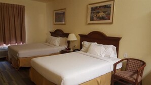 Habitación de hotel con dos camas individuales, una silla de madera, una mesita de noche y dos cuadros en la pared.