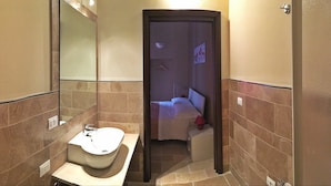 Un baño con lavamanos, espejo y una puerta que da a un dormitorio.