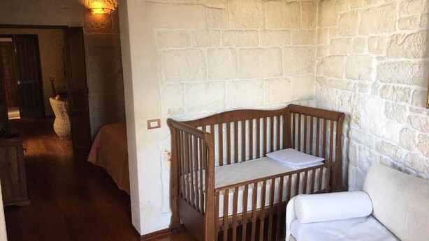 Una habitación con una cuna de madera, un sofá blanco y una pared de piedra.