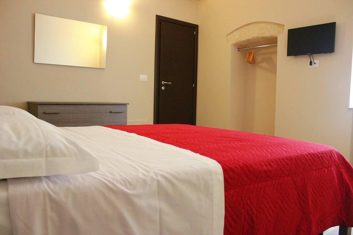 Ein Hotelzimmer mit einem Bett, einem Schminktisch, einer Tür, einem Fernseher und einem Duschbereich.