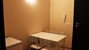 Una habitación pequeña con poca luz, una mesa blanca y cuatro sillas, una puerta negra y un teléfono blanco instalado en la pared.