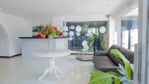 Un moderno vestíbulo de hotel con una mesa redonda blanca, un sofá de cuero negro y un separador de vidrio con flores de papel decorativas.