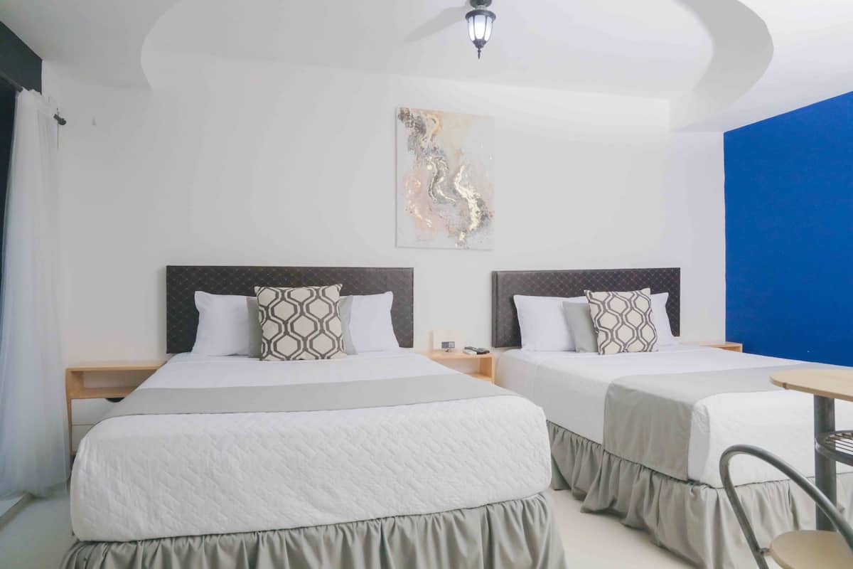 A hotel room with two beds, each with a patterned pillow and a bedside table.