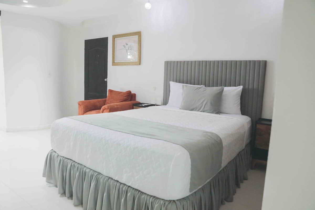 A modern bedroom with a large bed, a grey headboard, and a framed picture on the wall.
