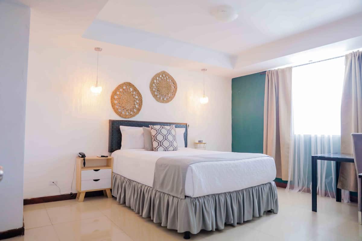 A hotel room with a bed, bedside table, lamp, and curtains.