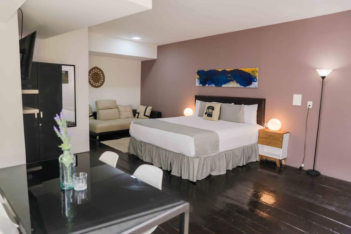 A modern hotel room with a large bed, bedside lamps, a desk with a vase, and a wall-mounted artwork.