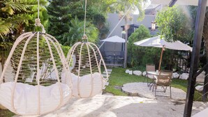 Un patio con sillas colgantes de mimbre blanco, mesas exteriores y sombrillas.