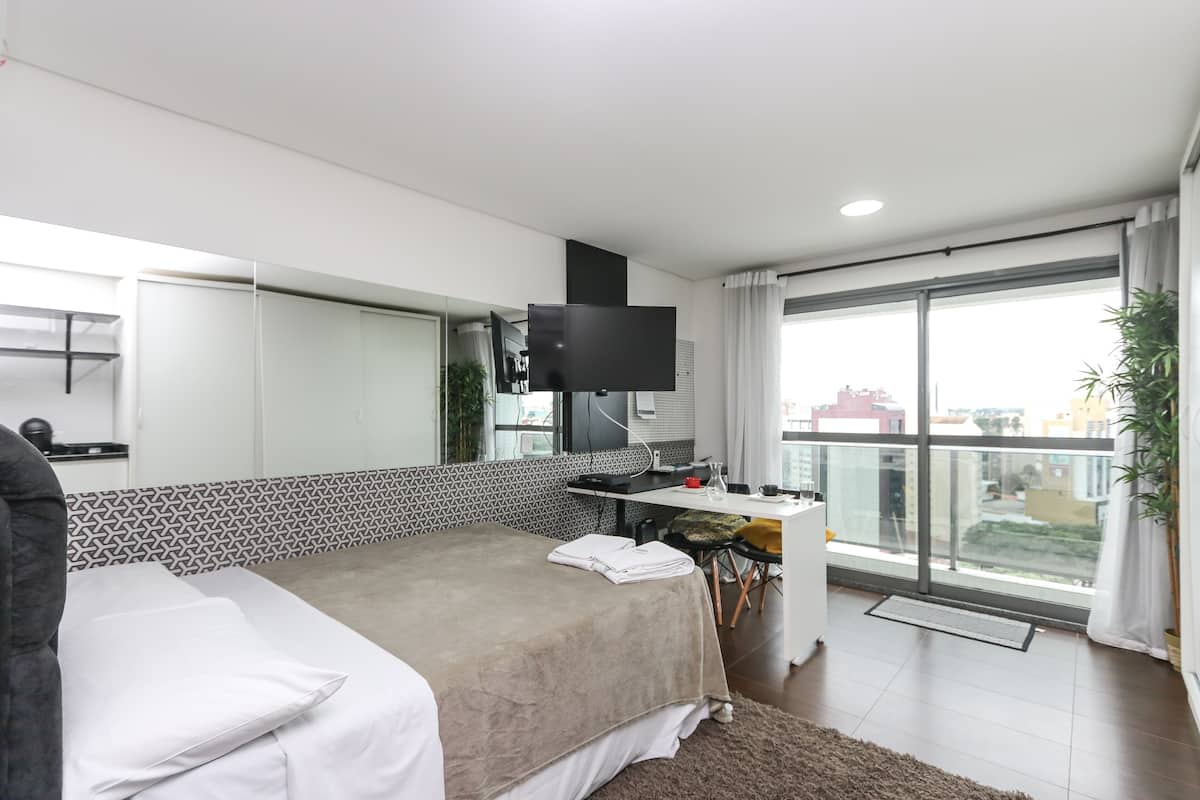 Quarto de hotel moderno com uma cama grande, uma escrivaninha, televisão de tela plana e varanda com vista.