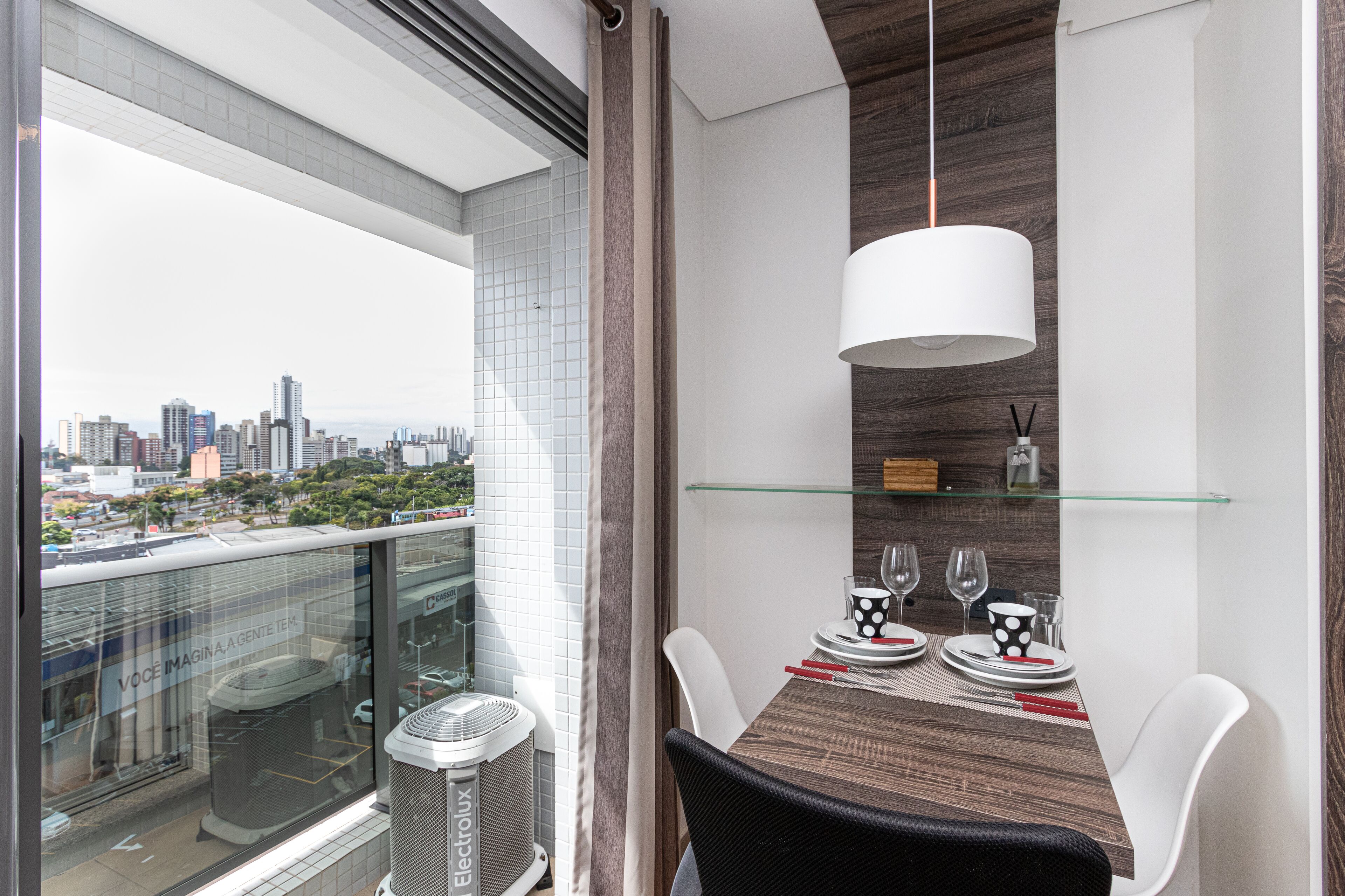 Uma zona de refeições moderna com vista para a cidade, uma mesa de vidro e um candeeiro pendente.