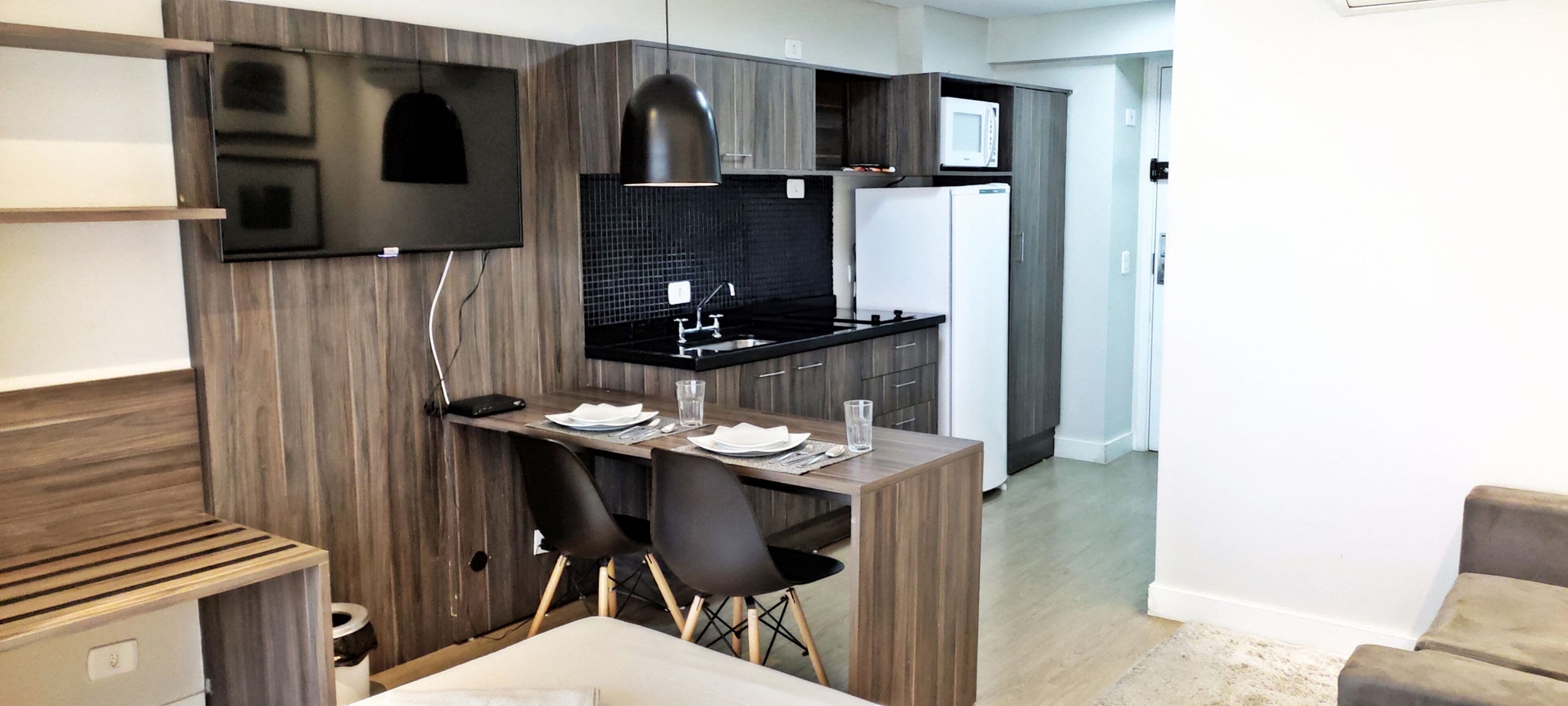 A modern kitchen with a black countertop, a microwave, and a refrigerator. There is a dining area with a table and chairs.