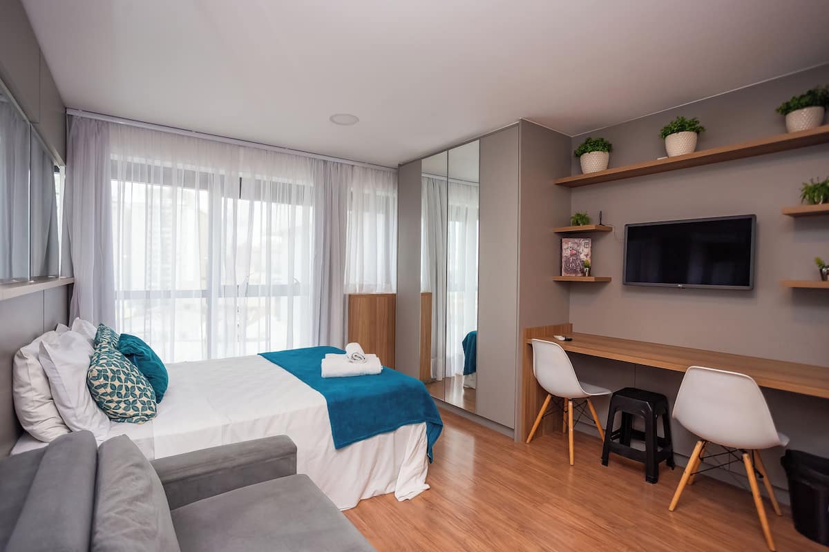 Quarto de hotel moderno com uma cama, uma escrivaninha, uma televisão e um espaço de estar.