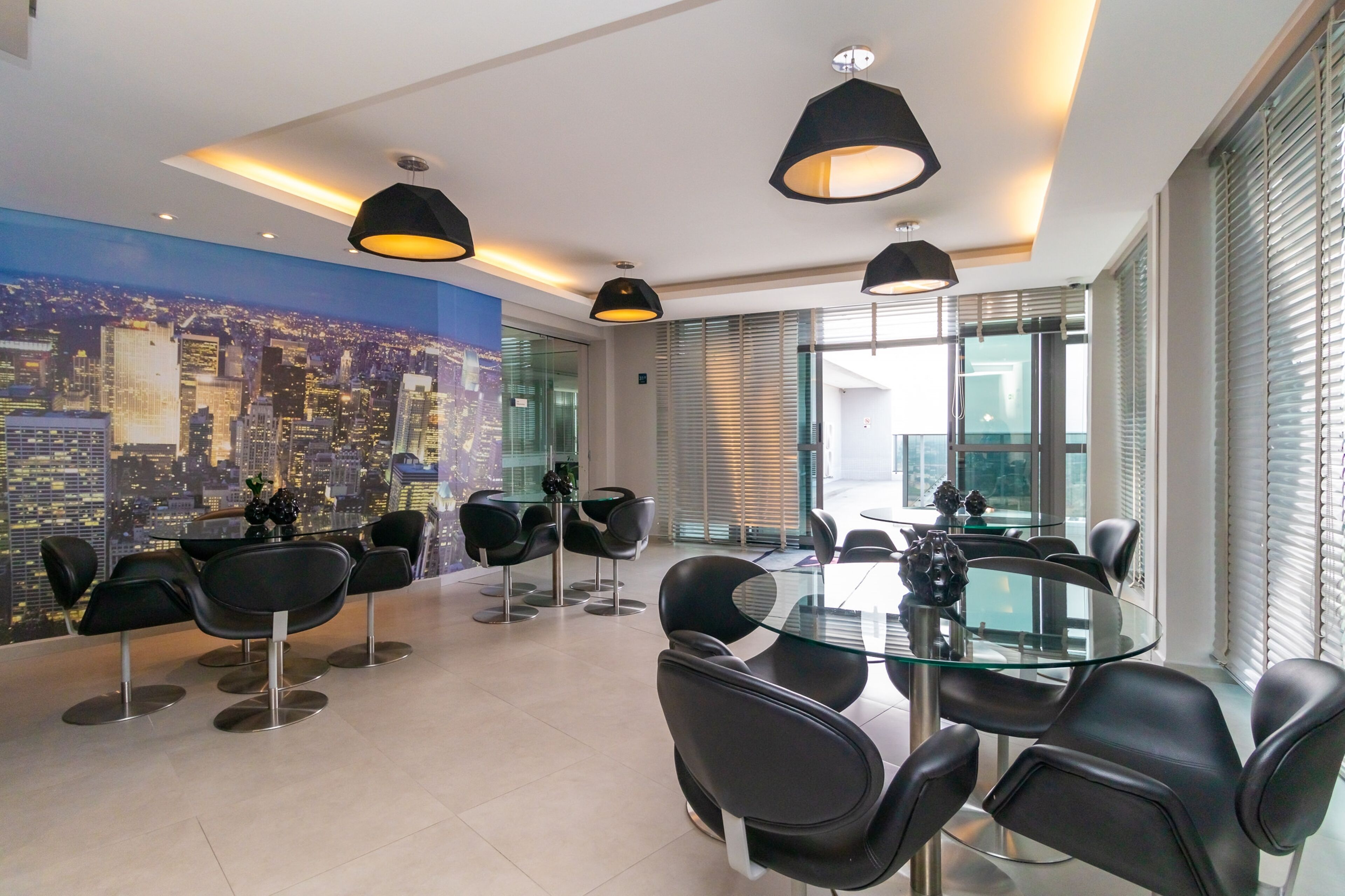 Una sala de conferencias moderna con una mesa de vidrio y sillas negras, ventanas amplias con persianas y un mural con vista a la ciudad.