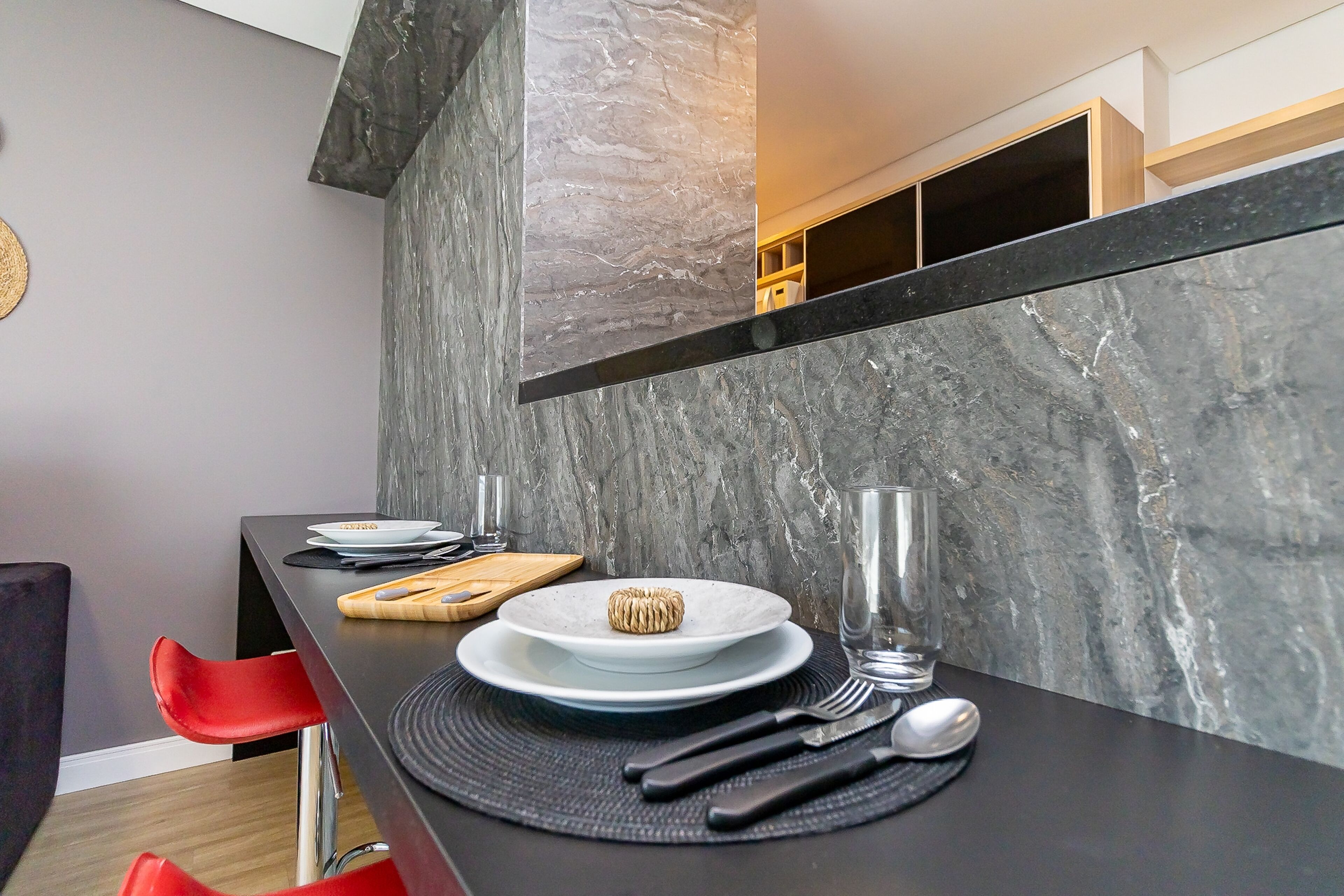A modern kitchen with a marble backsplash, a black countertop, and red chairs.