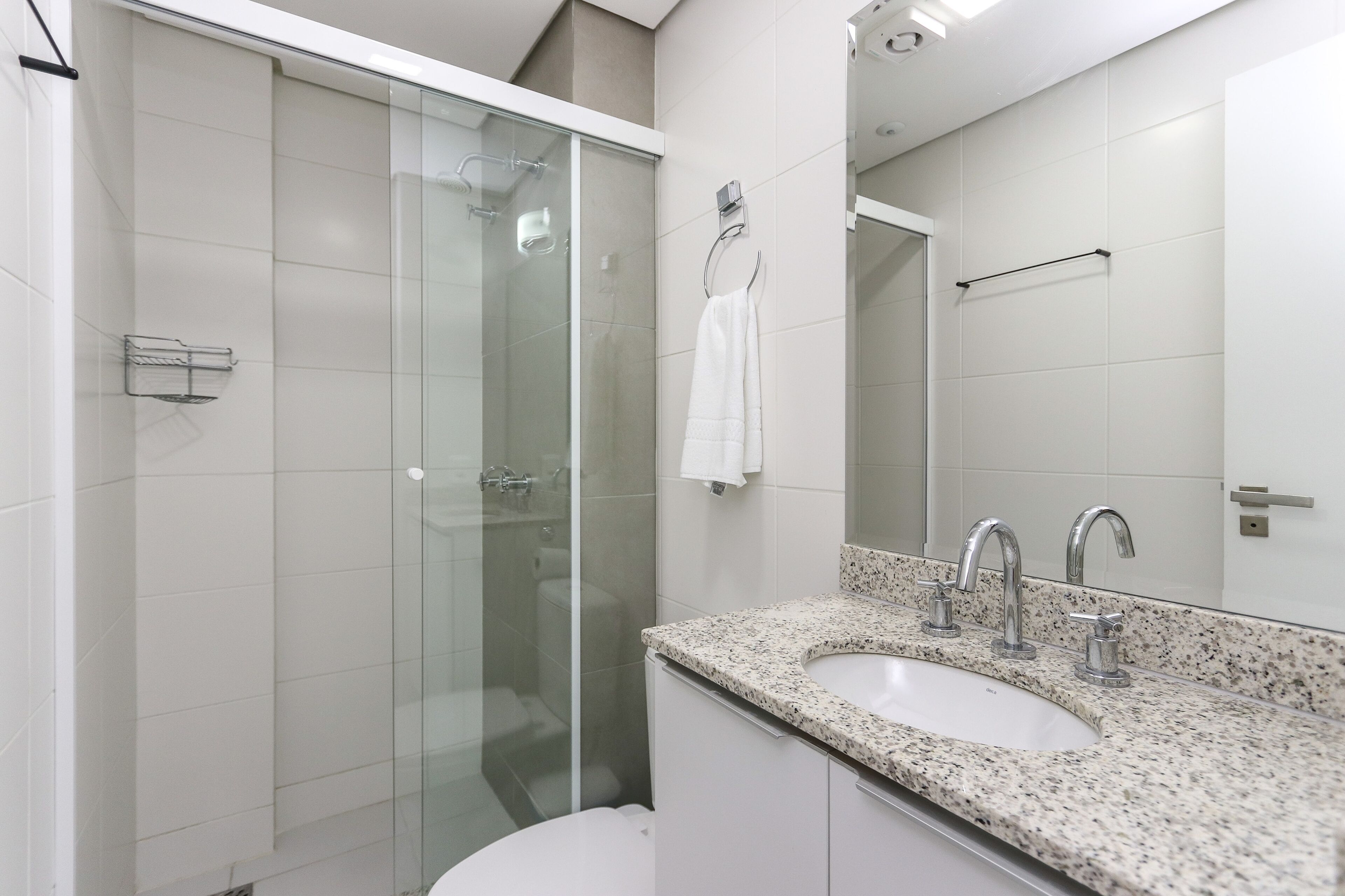 Een moderne badkamer met een douchecabine van glas, een wit wastafelmeubel met een granieten blad en een grote spiegel erboven.
