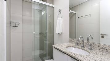 Een moderne badkamer met een douchecabine van glas, een wit wastafelmeubel met een granieten blad en een grote spiegel erboven.