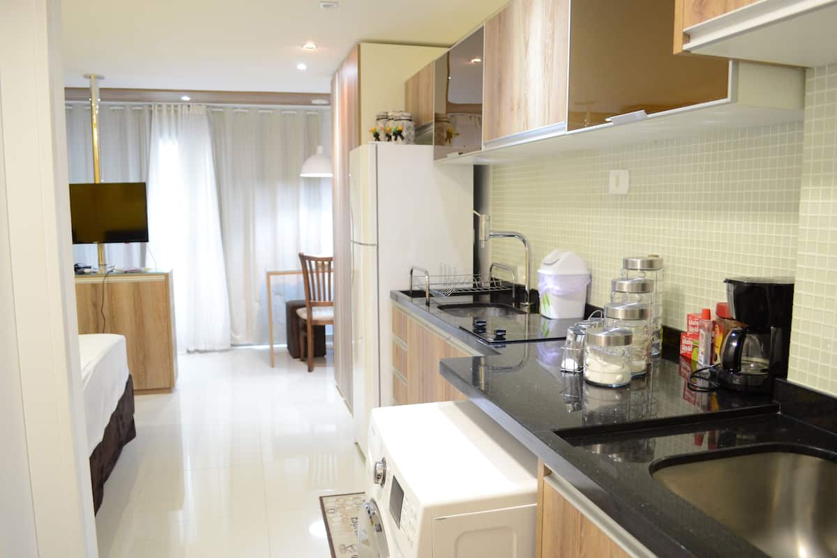 Cozinha moderna com bancada preta, pia de aço inoxidável e diversos eletrodomésticos, incluindo micro-ondas e cafeteira.