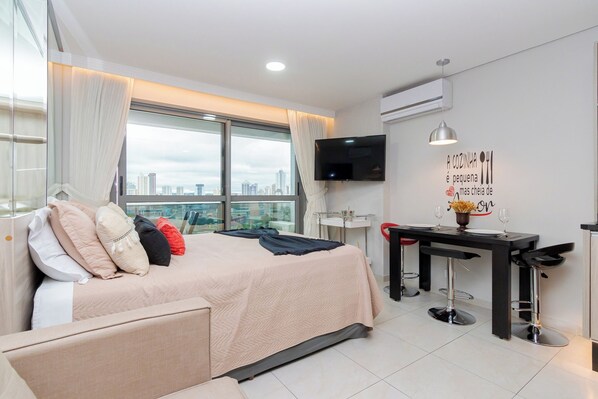 A modern hotel room with a bed, a desk, a TV, and a city view.
