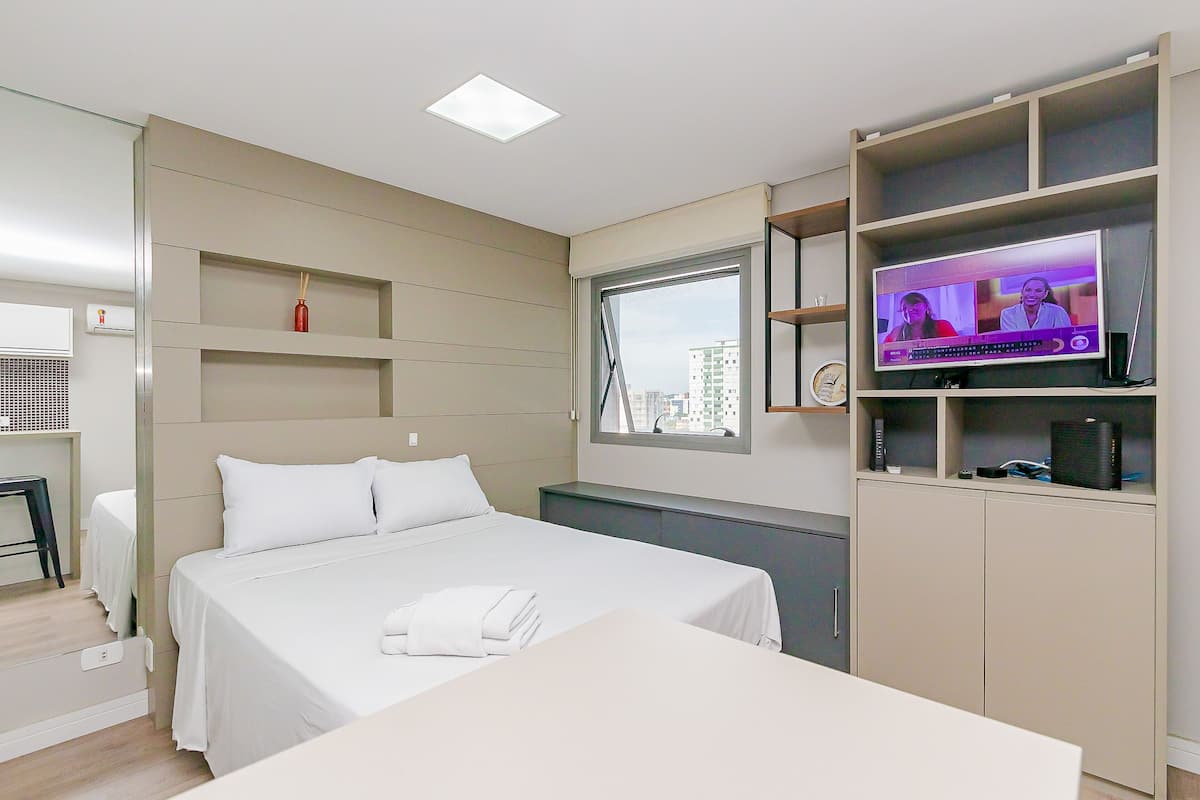 Quarto de hotel moderno com cama, TV, escrivaninha e janela com vista para a cidade.