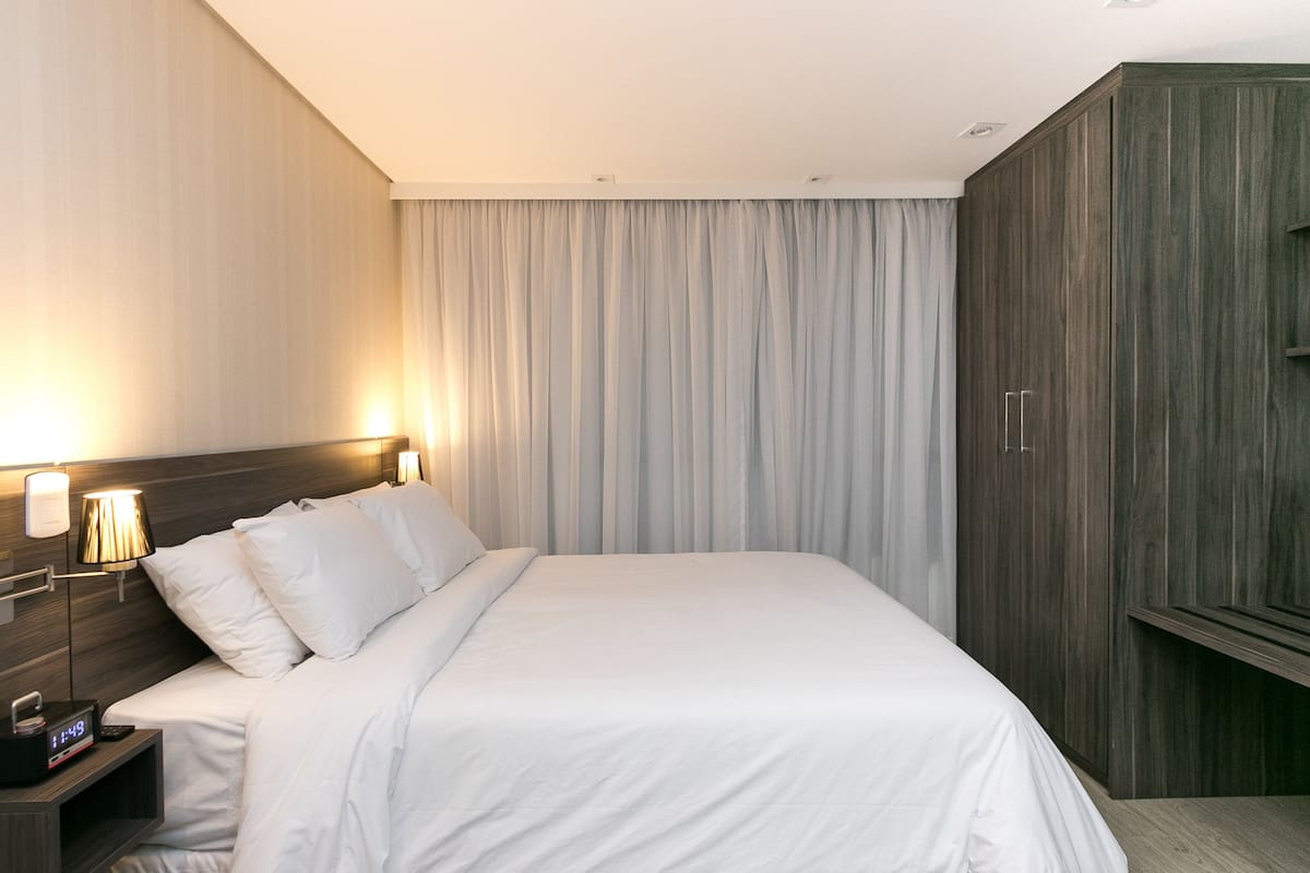 Quarto de hotel com uma cama, abajures, mesa de cabeceira e guarda-roupa.
