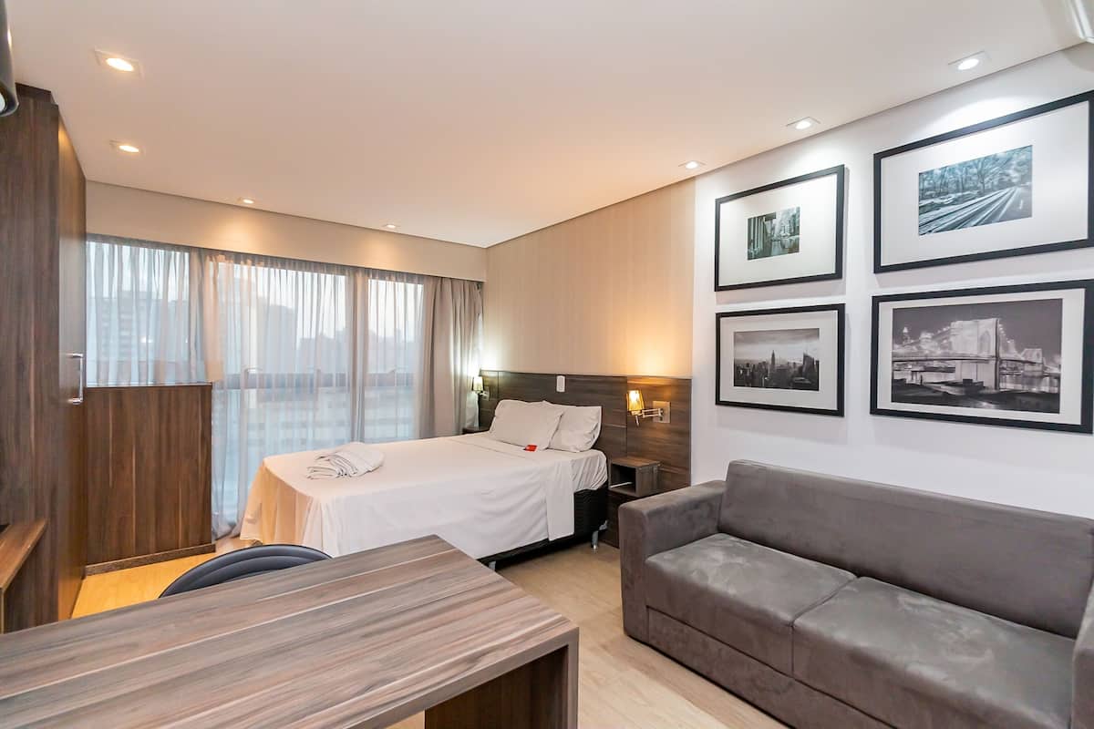 Quarto de hotel moderno com cama, sofá, escrivaninha e quadros na parede.