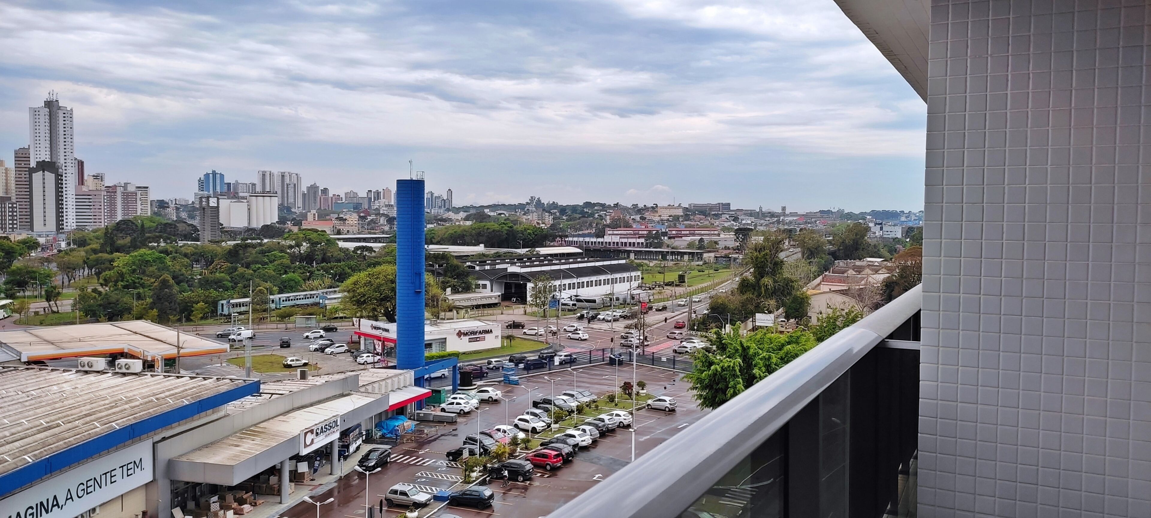 Un paysage urbain avec une tour bleue imposante, un parking et divers bâtiments, dont une station-service.