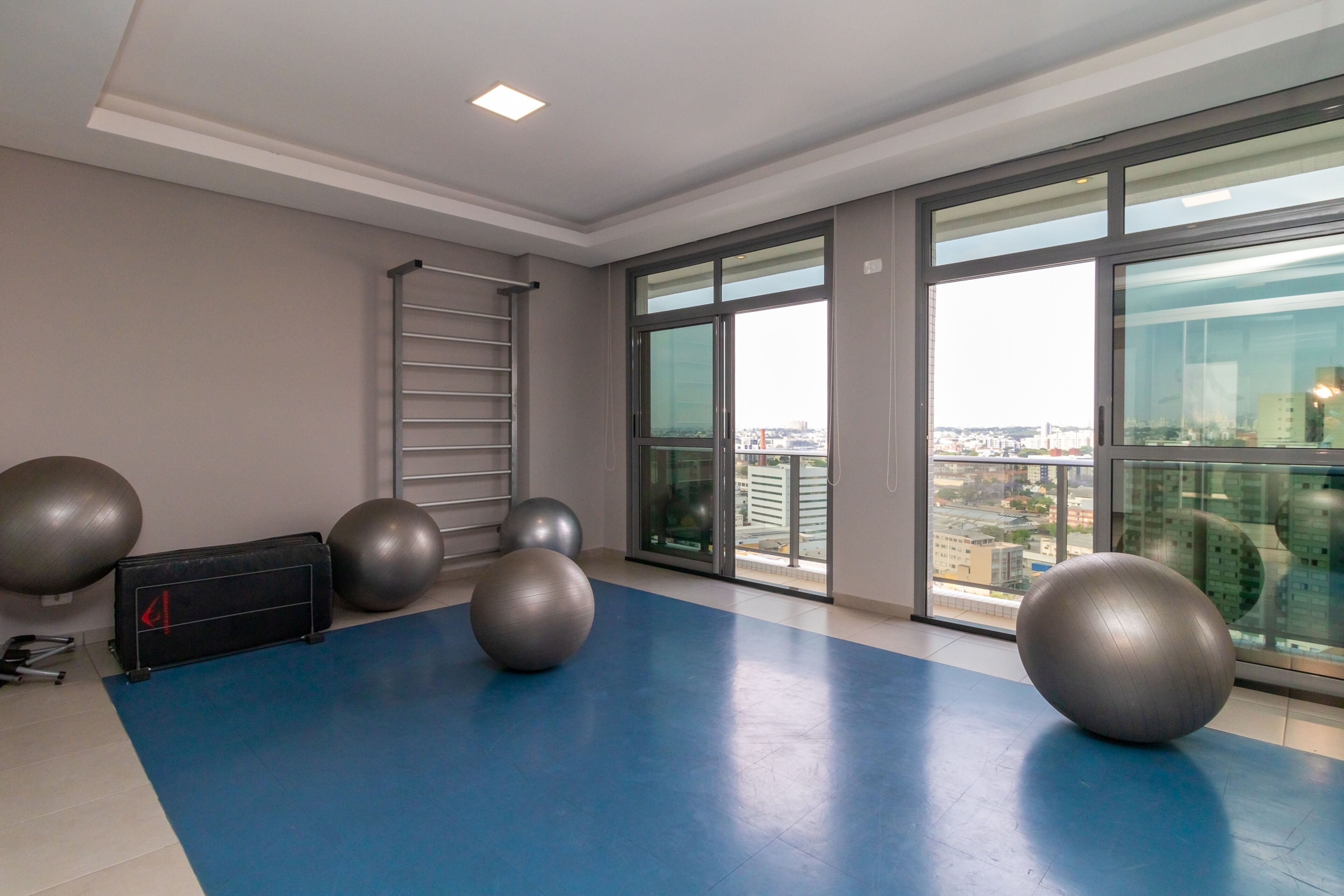 A gym with exercise balls, a ladder, and large windows offering a city view.