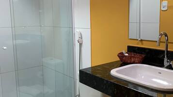 Un baño con cabina de ducha de vidrio, inodoro blanco, lavamanos negro con espejo superior y una pared de acento amarilla.