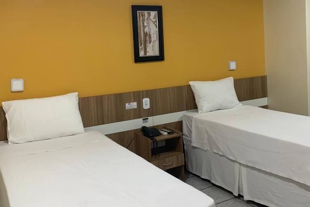 Ett hotellrum med två separata sängar, ett litet nattduksbord med en telefon, en inramad tavla på väggen och en lampa i taket.
