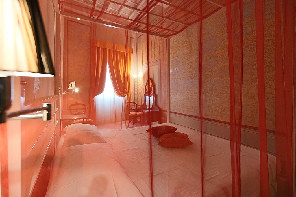 Een kamer met een bed, een stoel, een bureau en een raam met gordijnen.