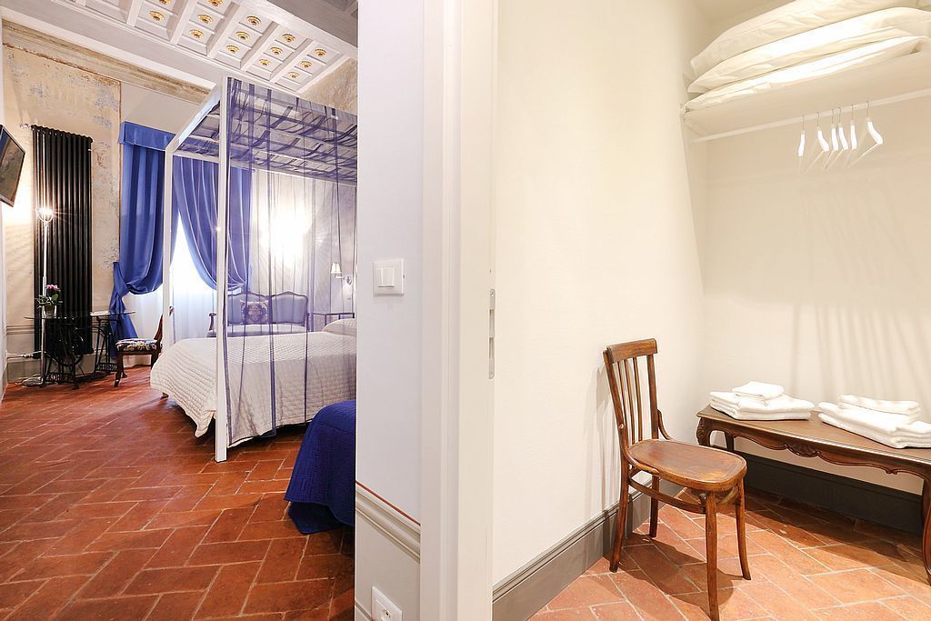 Quarto com cama de dossel, uma cadeira e uma mesa com toalhas dobradas.