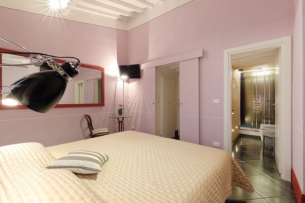 Una camera da letto con un letto, una scrivania, una sedia, uno specchio e un bagno parzialmente visibile attraverso una porta aperta.
