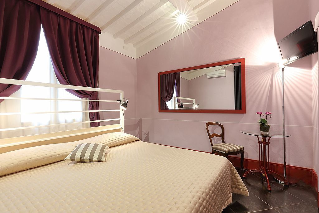 Une chambre à coucher comprenant un lit, une chaise, une petite table avec une plante, un miroir et un téléviseur fixé au mur.