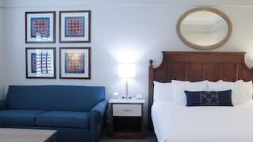 Ein Hotelzimmer mit einem Bett, einem Nachttisch mit Lampe, einem blauen Sofa und gerahmten Bildern an der Wand.