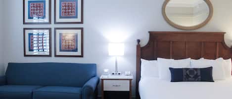 A hotel room with a bed, a nightstand with a lamp, a blue sofa, and framed pictures on the wall.