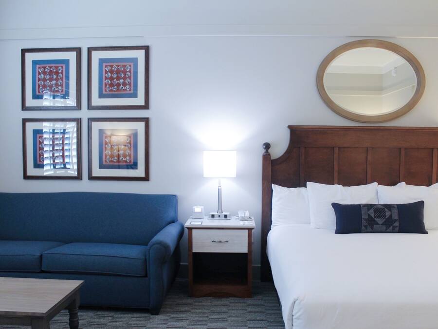 Een hotelkamer met een bed, een nachtkastje met een lamp, een blauwe bank en wanddecoratie.