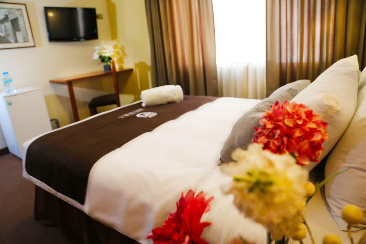 A hotel room with a bed, a desk, a television, and a window with curtains.