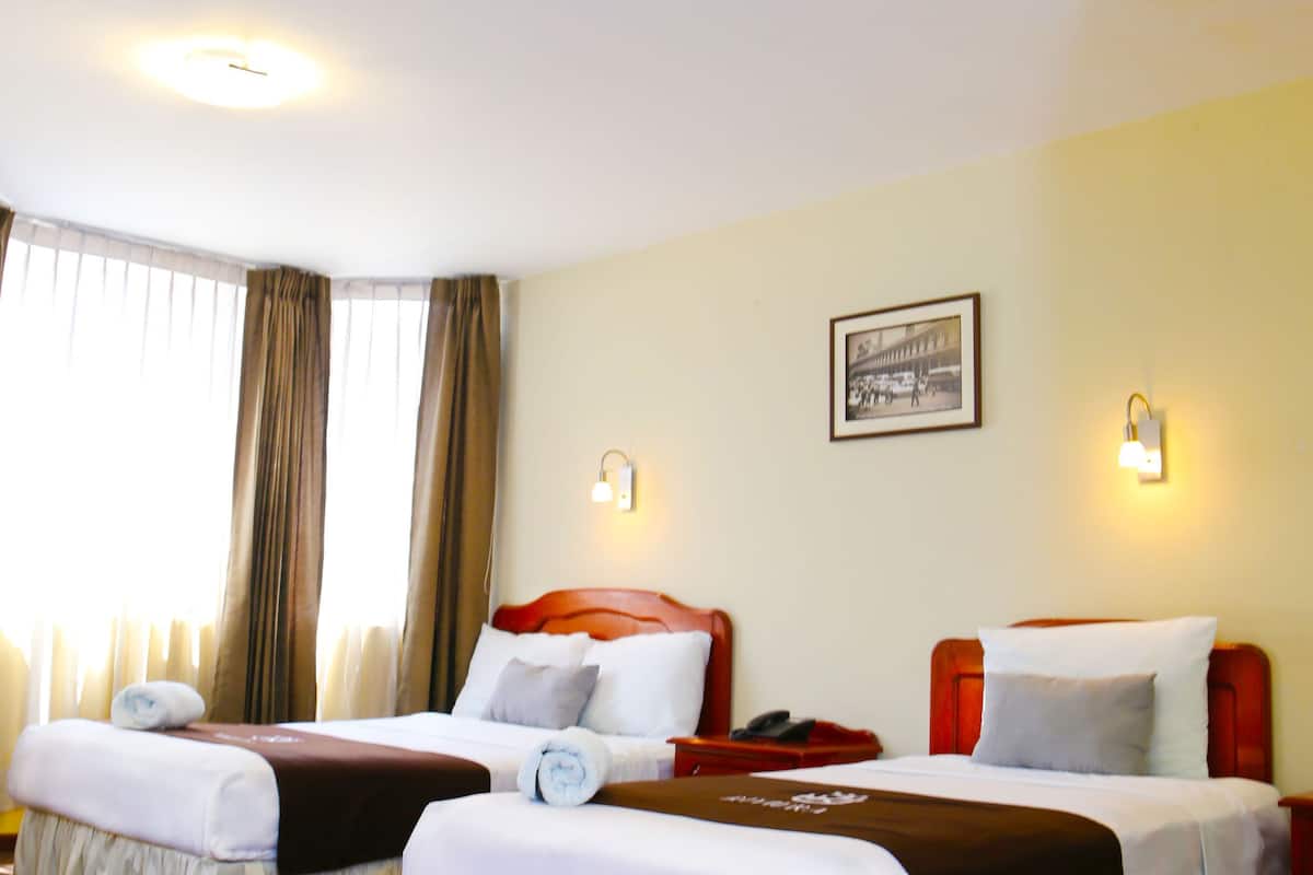 A hotel room with two beds, a nightstand, a framed picture on the wall, and a window with curtains.