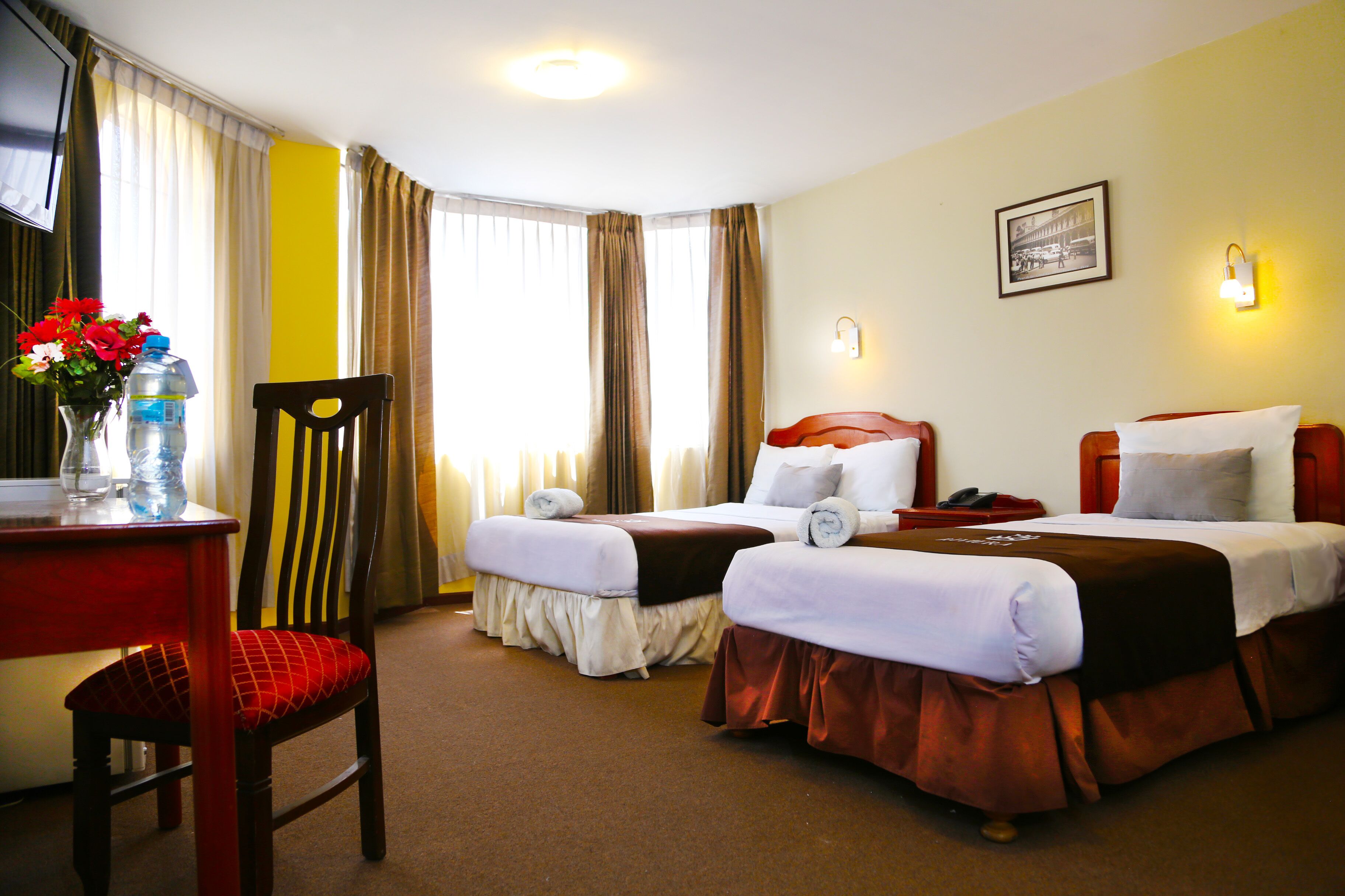 A hotel room with two beds, a desk with a chair, and a vase with flowers.