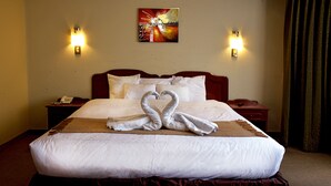 Una cama bien hecha con un arreglo de toallas en forma de corazón, un cuadro en la pared y dos lámparas fijadas a la pared.