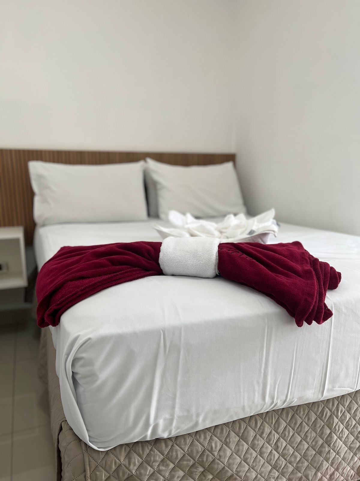 Una cama bien hecha con una colcha blanca y una manta roja doblada encima.