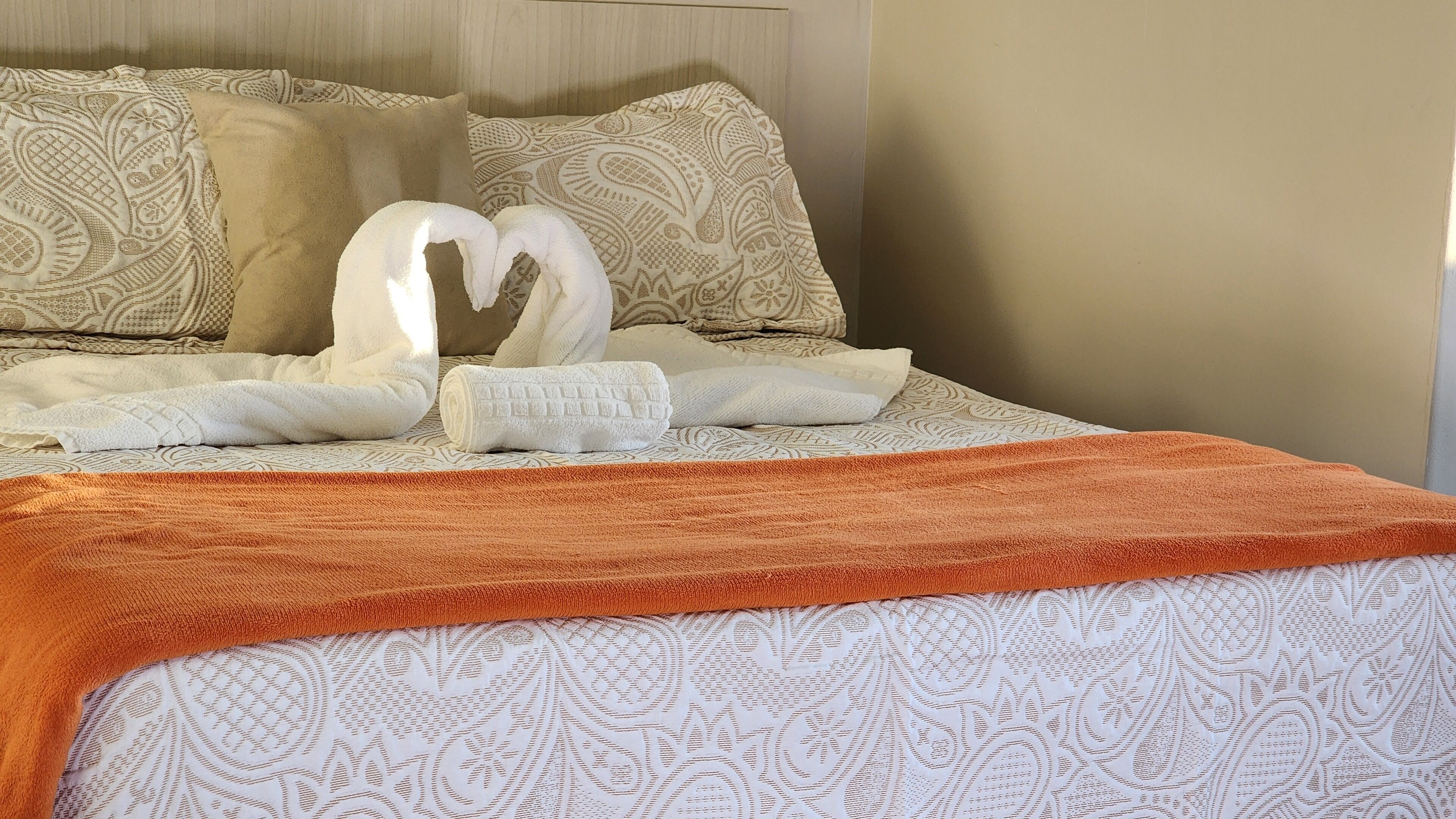 Een netjes opgemaakt bed met een bedsprei met een patroon, twee kussens met paisleimoppen, en een opgevouwen handdoek.